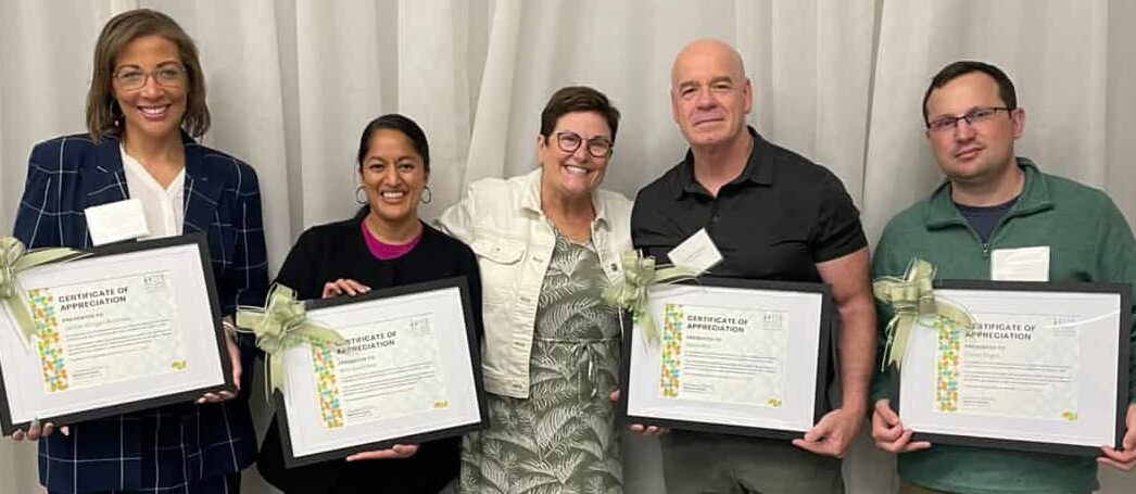 Five people in professional dress smiling while holding awards
